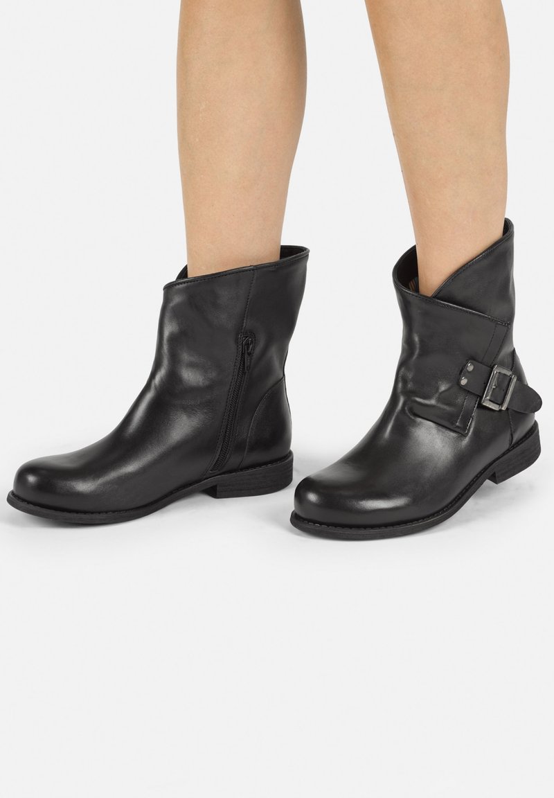 Black leather ankle boots with a zip closure, rounded toe, low heel, and decorative buckle detail on the side. Smooth texture, minimal design.
