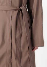 Brown trench coat with a smooth texture, featuring a tied belt at the waist and long, wide sleeves. The fabric appears lightweight and flexible.