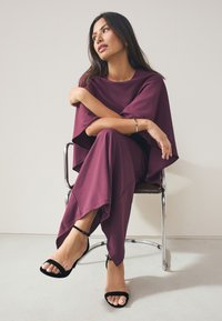 Bordni dvočlani outfit koji se sastoji od široke bluze s širokim rukavima i suženih hlača, upareni s crnim sandalama s trakicama, na kromiranoj stolici.