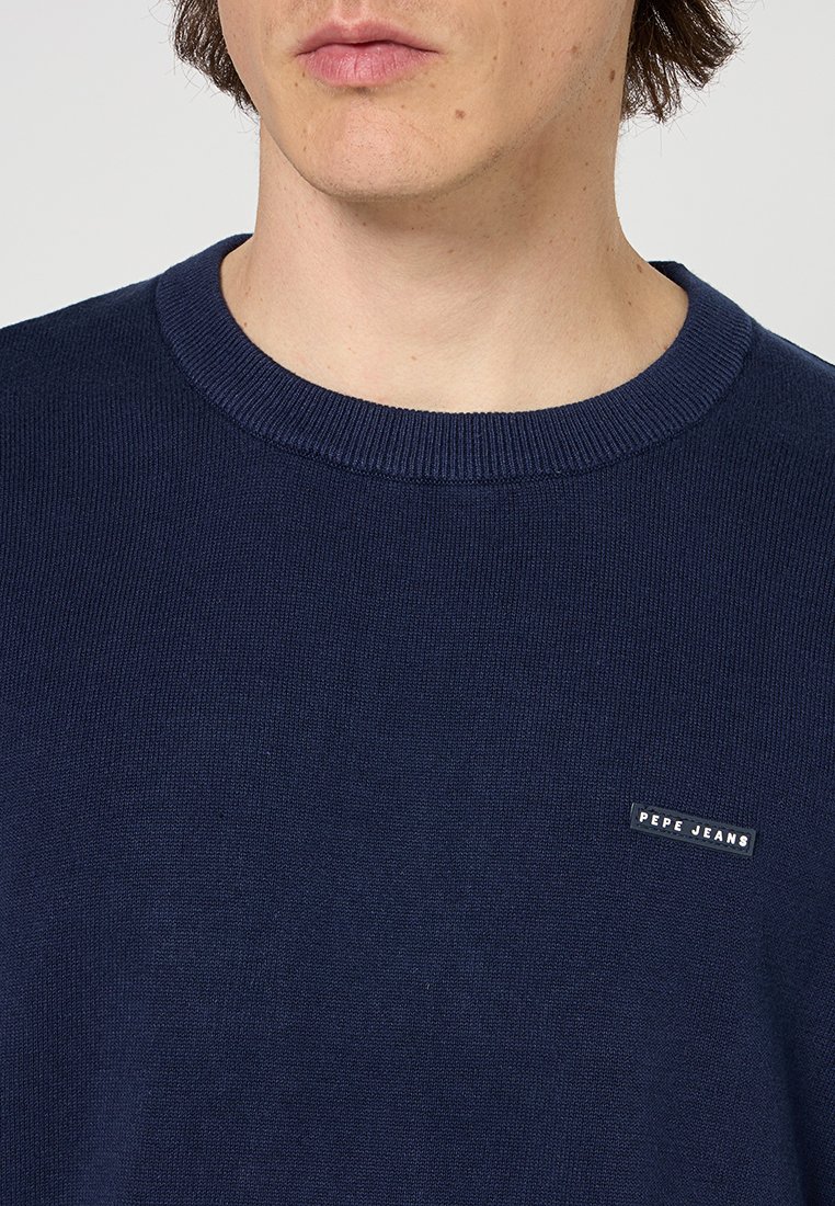 Maglione lavorato a maglia blu navy con collo rotondo a costine e un piccolo etichetta nera "Pepe Jeans" sul petto. Texture morbida e design attillato.