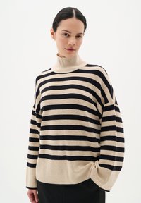 Pulover pe dungi în bej și negru, cu guler înalt, croială lejeră și textură răsucită. Dungile sunt distribuite uniform pe toată suprafața.