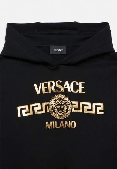 Crna dukserica s kapuljačom sa zlatnim Versace logotipom, amblemom glave Meduze i geometrijskim uzorcima iznad teksta „Milano“ sprijeda.