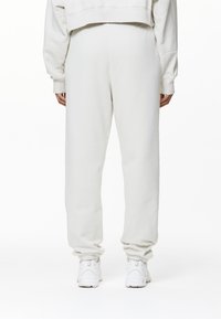 Witte, zachte joggingbroek met een relaxte pasvorm, elastische tailleband en gathered cuffs. Afgewerkt met witte sneakers, gezien van achteren.
