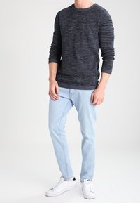 Suéter de punto azul marino con patrón texturizado, cuello redondo y mangas largas, combinado con jeans azul claro y zapatillas blancas.