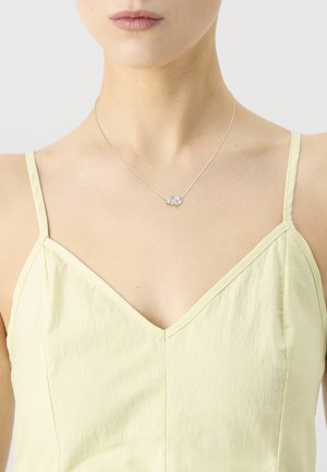 Silver necklace featuring a small, cluster design with clear stones, worn on a model with a light yellow, sleeveless top.