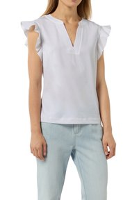 White cotton top with ruffled sleeve accents, V-neckline, and textured stitching along the neckline. Paired with light blue jeans.