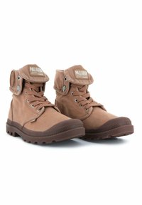 Bottes en toile marron avec un col matelassé, un système de laçage à l'avant et une fermeture par bouton-pression. Semelle en caoutchouc avec bords texturés et détail du logo sur la languette.