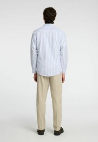 Pitkähihainen, vaaleansiniselle ja valkoiselle raidoitettu paita, pyöristetty helma, napitettava hiharesori ja muotoiltu malli, yhdistettynä beigen värisiin housuihin.