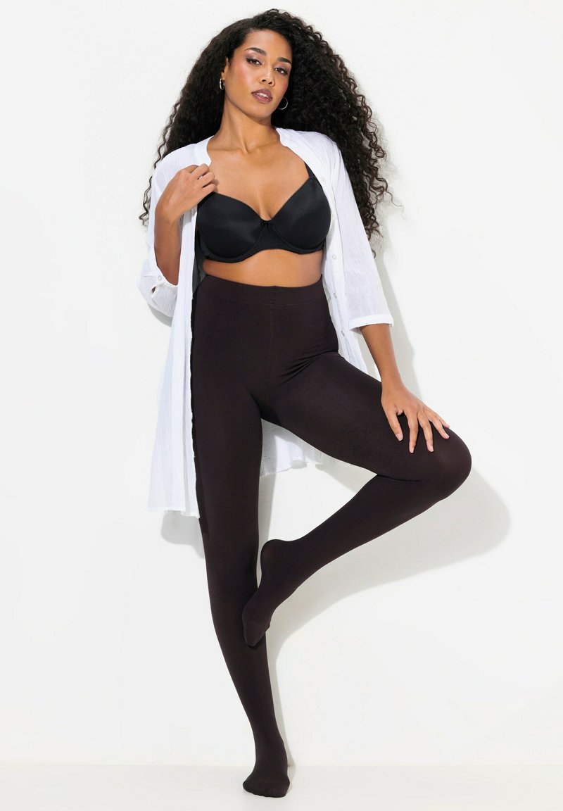 Leggings neri opachi realizzati in materiale elasticizzato, abbinati a un reggiseno neri aderente e una camicia bianca morbida, evidenziando la silhouette.