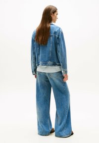 Giacca di denim blu sbiadito con vestibilità rilassata, abbinata a jeans blu a gamba larga. L'outfit presenta una camicia bianca testurizzata sotto.