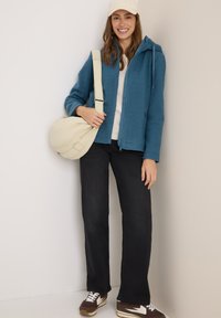 Veste en polaire bleue avec capuche, pull crème, pantalon noir et baskets marron avec accents blancs. Porte un sac à bandoulière beige.