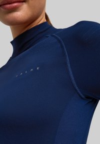 Granatowa sportowa koszulka z długim rękawem wykonana z gładkiego, elastycznego materiału, z wysokim kołnierzem i minimalistycznym logo na piersi.