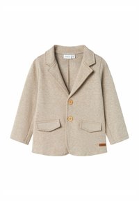 Blazer beige in maglia con rever a punta. Due tasche frontali, tre bottoni e un piccolo etichetta in pelle sull'orlo. Texture morbida, design casual.