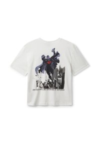 Bílý bavlněný tričko s volným střihem, na kterém je grafika Supermana v akci, umístěná na pozadí městského panoramatu.