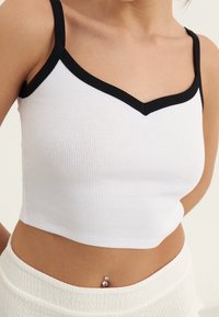 Haut court blanc côtelé avec un col en V noir et des bretelles fines. Texture notable et coupe ajustée.