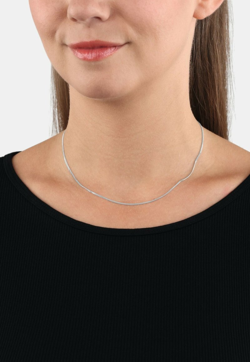 Collana in argento con un design liscio e flessibile. Si posiziona vicino al collo, completando un top nero a coste.