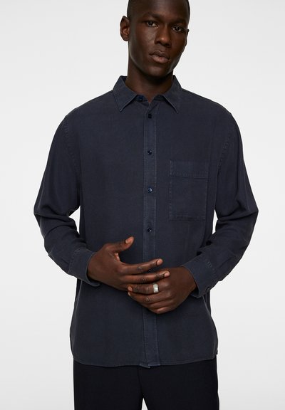 Dark navy button-up shirt in lightweight fabric, featuring a chest pocket, long sleeves, and dark buttons. Smooth texture and relaxed fit.