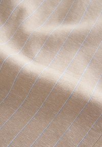 Bež tkanina s teksturiranim tkáním, s tankim plavim prugama koje se protežu okomito. Materijal izgleda mekan i lagano naboran.