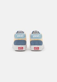 Zapatillas de caña alta VANS con parte superior de pana amarilla, acentos azules, suela blanca y logotipo rojo en el talón. Tejido texturizado para mayor agarre.