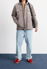 Graue Cord-Jacke mit zwei Brusttaschen, kombiniert mit hellblauen, lockeren Jeans und roten Turnschuhen mit weißen Streifen.
