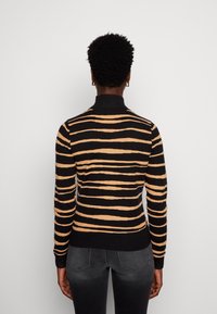 Pull à col roulé rayé noir et fauve avec manches longues et poignets côtelés. Texture en maille lisse, coupe ajustée et motif de couleur contrastée.