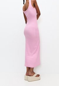 Robe sans manches rose au design ajusté et à l'ourlet au genou. Portée avec des sandales à plateforme beiges, possédant une texture lisse.