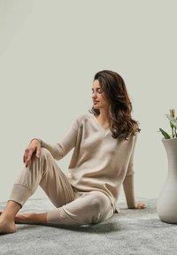 Beige knitted loungewear set with a V-neck sweater and tapered pants, featuring ribbed accents and soft texture, paired with a white vase.