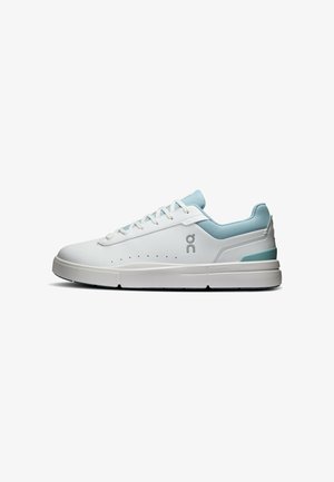 Baskets basses blanches avec col rembourré bleu clair, lacets blancs, perforations sur le côté et logo sur le côté au-dessus d'une semelle épaisse.