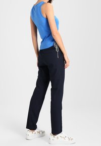 Niebieska, bezrękawnikowa koszulka zestawiona z ciemnogranatowymi spodniami i białymi trampkami z zabawnym printem zwierzęcym. Widok z tyłu pokazuje dopasowany krój.