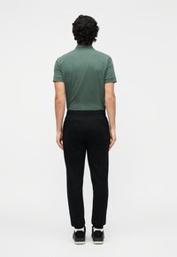 Zelená polokošeľa s krátkym rukávom v kombinácii s čiernymi zúženými teplákmi. Oblečenie má jednoduchý dizajn a mäkkú bavlnenú textúru.