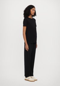 Black short-sleeve t-shirt with a subtle graphic, paired with loose black pants and light-colored sneakers with multicolored stripes.