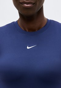 Κοντινή λήψη ενός ατόμου που φοράει σκούρο μπλε μπλουζάκι Nike με λευκό λογότυπο Nike Swoosh στο κέντρο κάτω από το λαιμό.