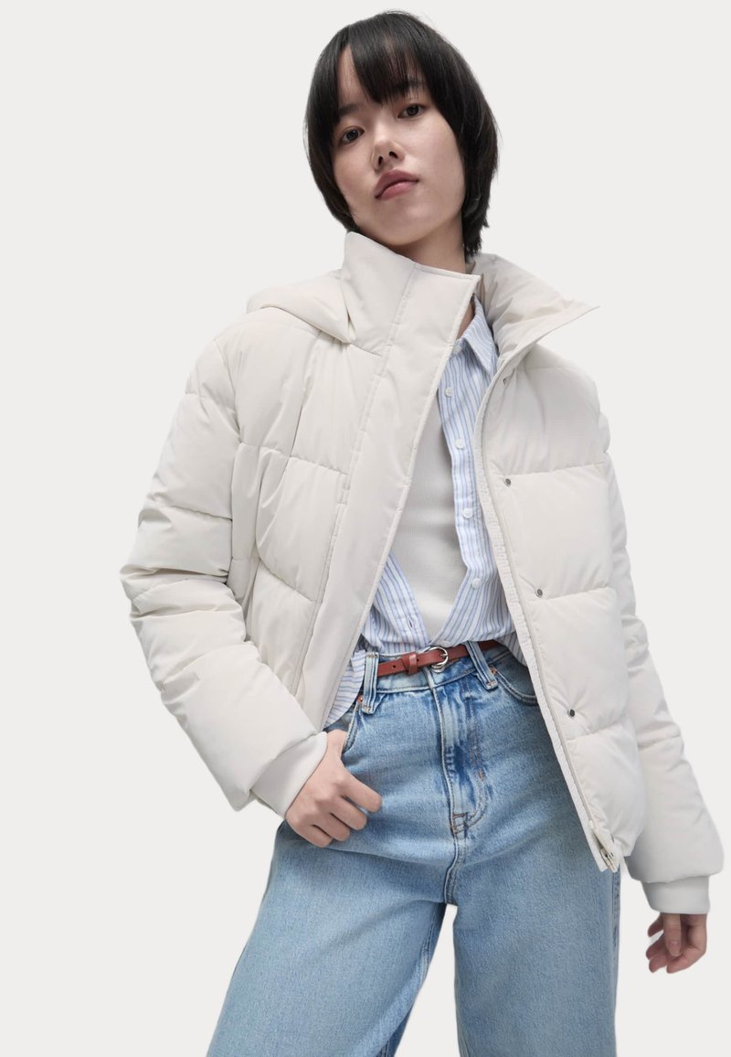 Dikke crème jas met een capuchon, met een ritssluiting aan de voorkant, een gewatteerd ontwerp en elastische manchetten, gecombineerd met lichtblauwe hoge taille jeans.