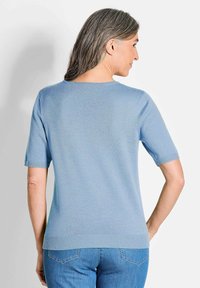 Helle blaue kurzärmlige Sweater mit rundem Ausschnitt und geripptem Saum. Glatte Textur, taillierte Passform, sichtbare Nähte und Rückansicht sind dargestellt.