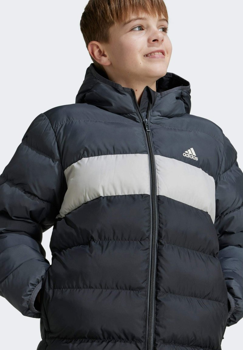 Chaqueta de invierno acolchada en gris oscuro con una franja gris claro. Cuenta con un cierre frontal de cremallera y una capucha. Está hecha de material suave y brillante.