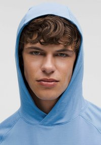 Lichtblauwe hoodie met een textuurpatroon, met een grote capuchon en een relaxte pasvorm. De stof lijkt glad en lichtgewicht.