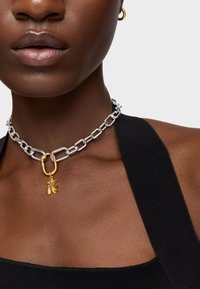 Naszyjnik łańcuszkowy z naprzemiennymi srebrnymi i złotymi ogniwami, z zawieszką w kształcie kwiatu, ozdobioną małym różowym akcentem.