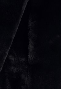 Schwarzer Kunstfellstoff mit einer weichen, plüschigen Textur. Der Stoff hat eine glatte Oberfläche und eine tiefe, satte Farbe, die Variationen in der Schattierung aufweist.