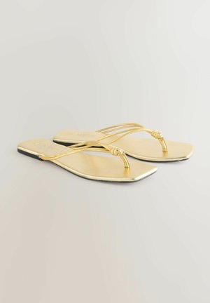 Sandales plates dorées avec un design de bride nouée et une finition métallique lisse. Forme à bout carré, brides minimalistes et une semelle noire.