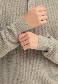Light gray knitted sweater with ribbed cuffs and a buttoned collar. Textured fabric with a relaxed fit and soft, cozy appearance.