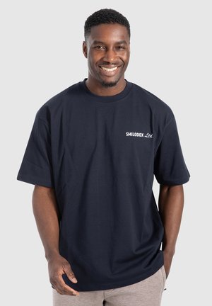 Marineblå T-shirt med korte ærmer og rund hals, prydet med hvid "SMILODOX Ltd." tekst på venstre bryst. Blødt bomuldsstof, afslappet pasform.