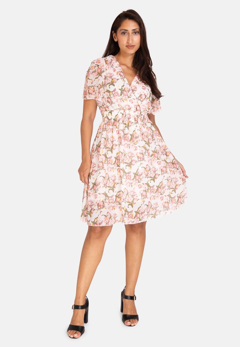 Blommig omlotkjol i rosa och vit tyg med korta puffärmar, elastisk midja och kjol i knä längd. Parat med svarta klacksandaler.