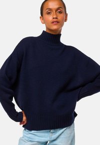 Pull à col roulé navy à coupe ample, avec des poignets et un ourlet côtelés, fabriqué en un tissu tricoté doux et texturé. Assorti à un jean en denim bleu clair.