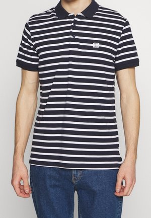 Polo rayé bleu marine et blanc avec un col, trois boutons et un petit écusson logo sur la poitrine gauche, fabriqué en coton, à manches courtes.