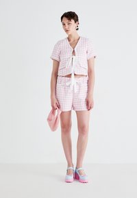 To-delt antrekk som består av en kortermet, lyserosa, teksturert topp med knyting, sammen med matchende shorts. Rosat veske og multikolorert sko.