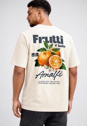 Man wearing cream-colored t-shirt with large orange fruit graphic and text reading "Frutti d'Italia Amalfi" on the back.