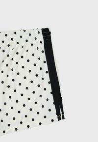 Tissu blanc avec des pois noirs et une bande noire verticale sur le côté droit, avec une ceinture élastique en haut.