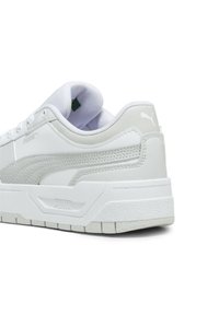 Baltas sneakers ar teksturētu ādas augšdaļu, mīkstiem apmalēm un logotipa akcentiem. Piedāvā masīvu gumijas zoli ar rakstainu protektoru.