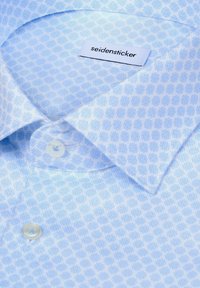 Chemise bleu clair avec un petit motif géométrique, boutons blancs et étiquette "seidensticker" à l'intérieur du col.