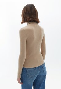 Beige gestreifter Rollkragenpullover mit langen Ärmeln, tailliertem Schnitt und glatter Textur, kombiniert mit hochtaillierten blauen Jeans.